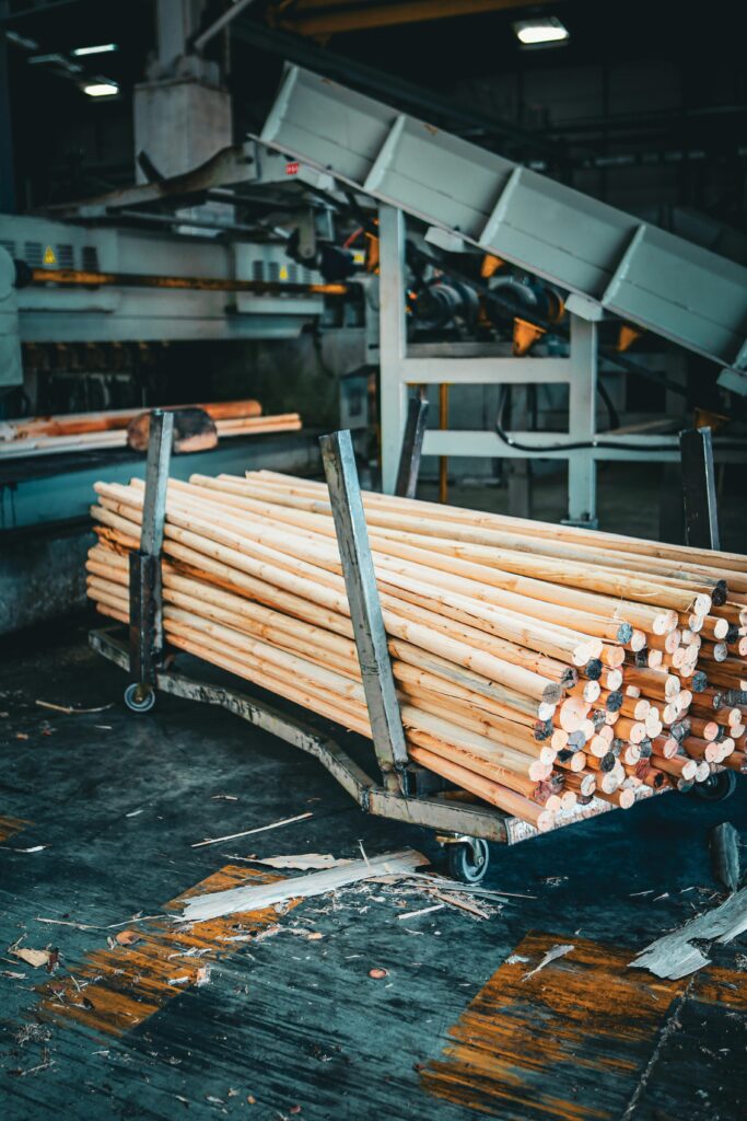 A stack of wooden dowels on a cart in an industrial factory setting.